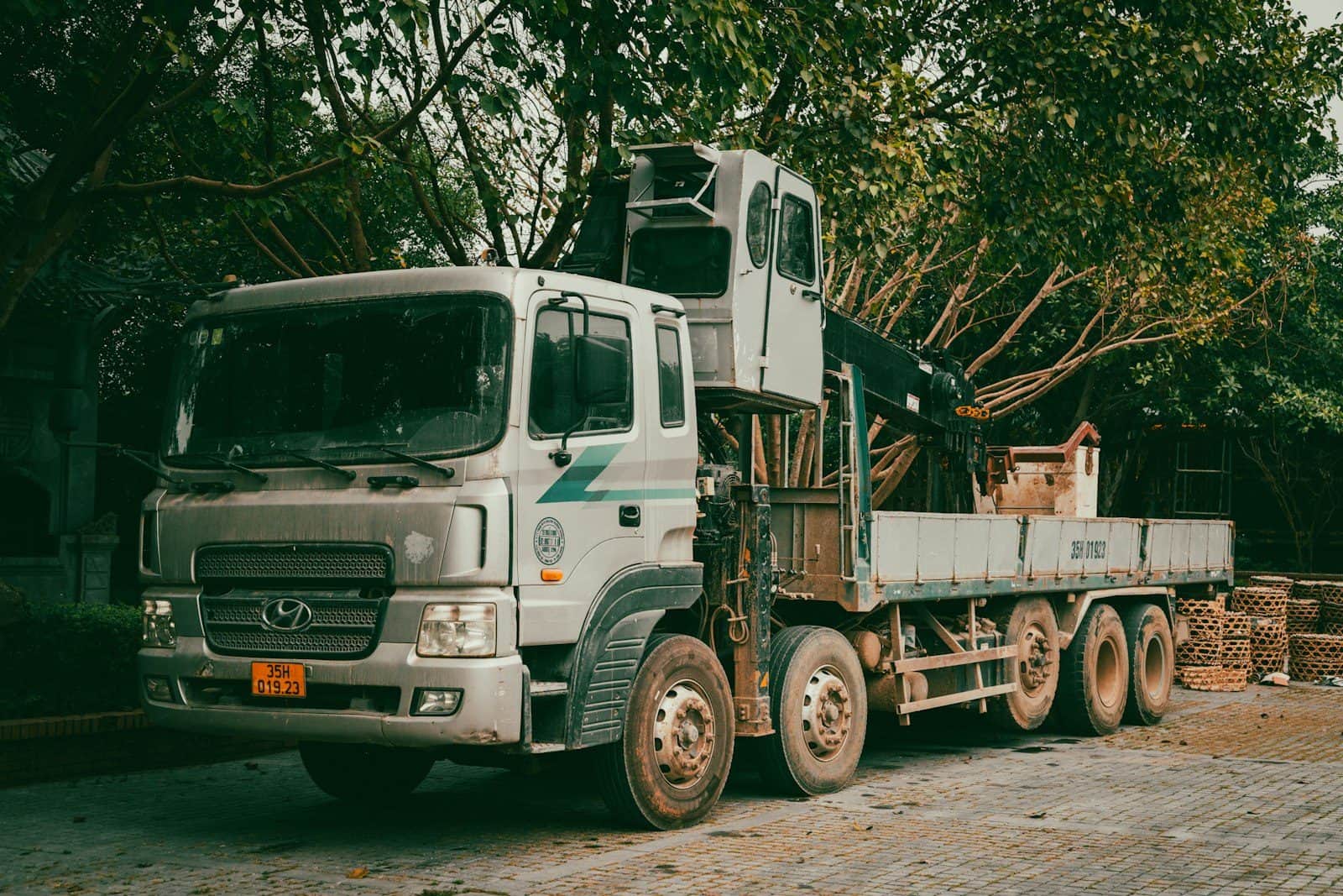 A truck-mounted crane parked with its boom stowed over a clear flat bed
