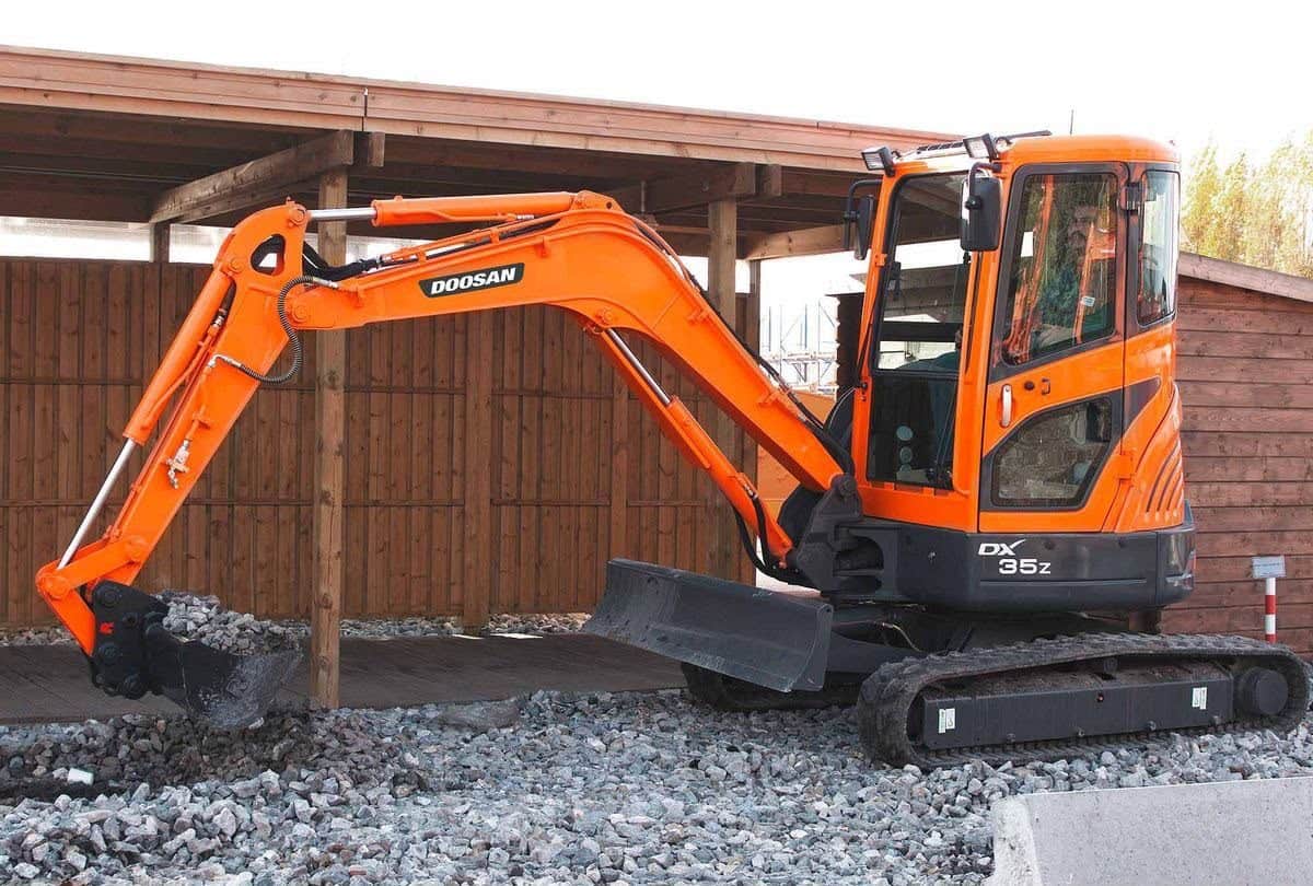 A compact tracked excavator with its arm folded, parked on open ground