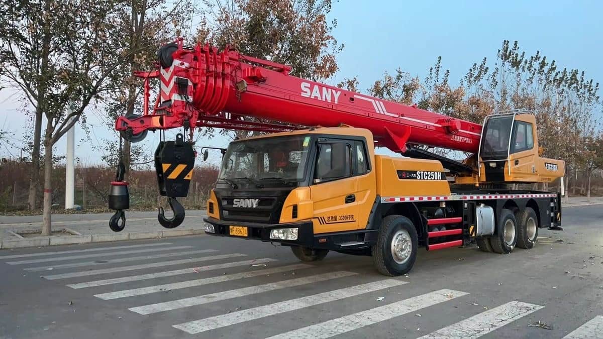 A truck-mounted telescopic crane parked at the kerb with its boom raised and hook block lowered