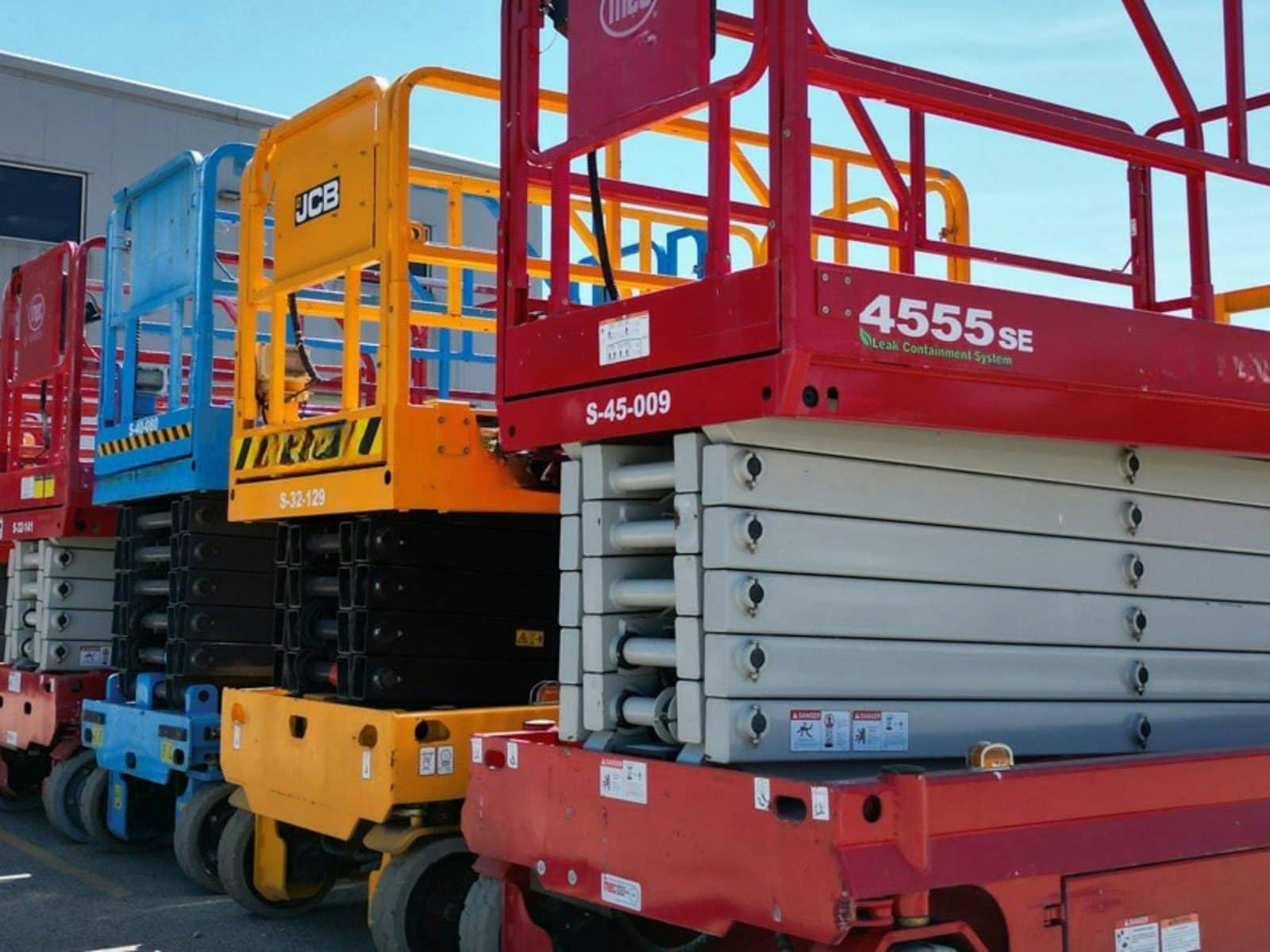 Scissor lifts lined up in an equipment yard with their platforms lowered
