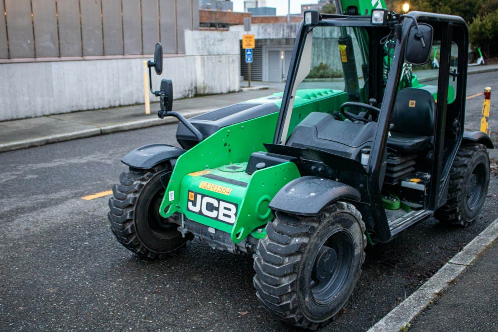 A compact telehandler with its telescopic boom lowered, parked kerbside