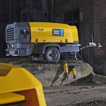 A towable site air compressor with pneumatic breakers laid out in front of it