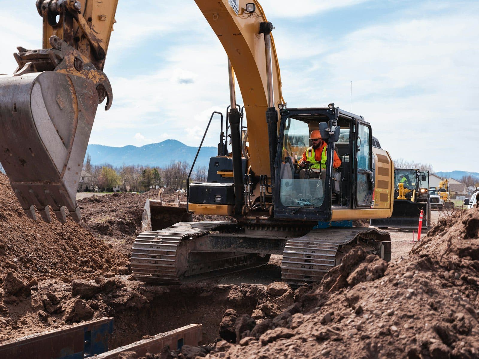An excavator cutting a trench with an operator in high-visibility gear