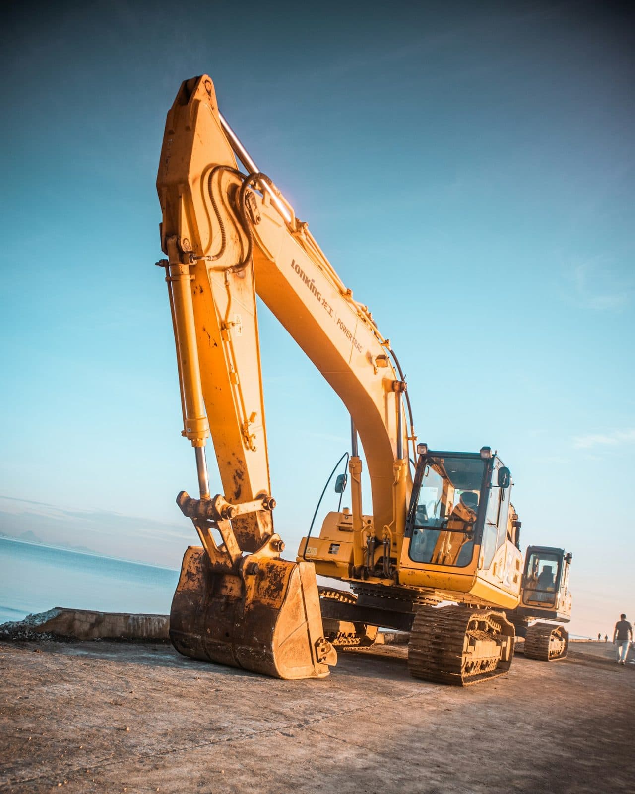 A tracked excavator standing on open ground at golden hour